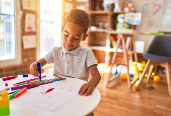 Beautiful african american toddler drawing using paper and marker pen at kindergarten